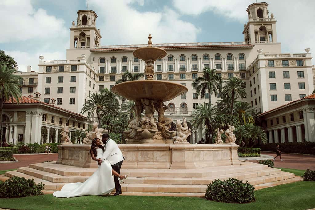 Elegant wedding couple kissing in front of a grand hotel fountain in Palm Beach.