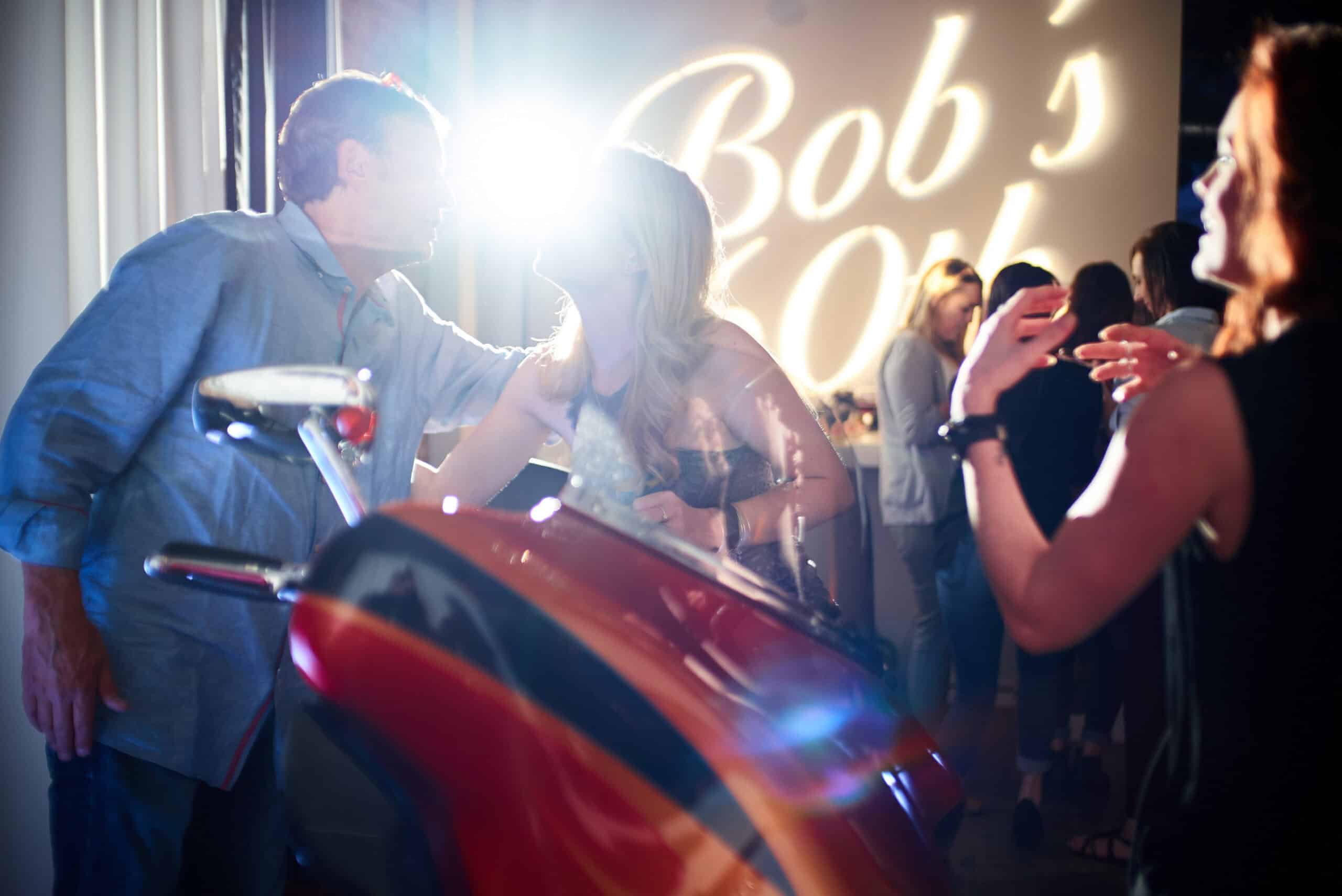 Guests dancing and socializing at a lively event with bright lighting and a neon sign.