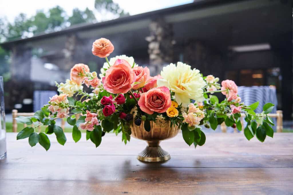 Elegant floral centerpiece with roses and carnations in a gold vase for event decor.