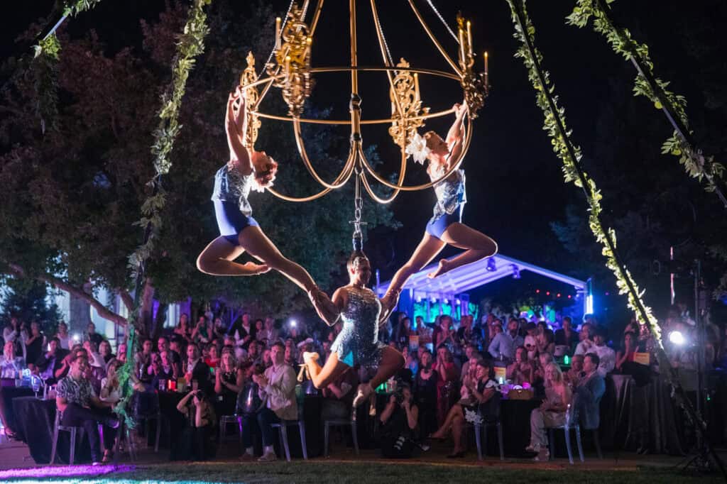 Performers hanging from a chandelier at a charity gala event.