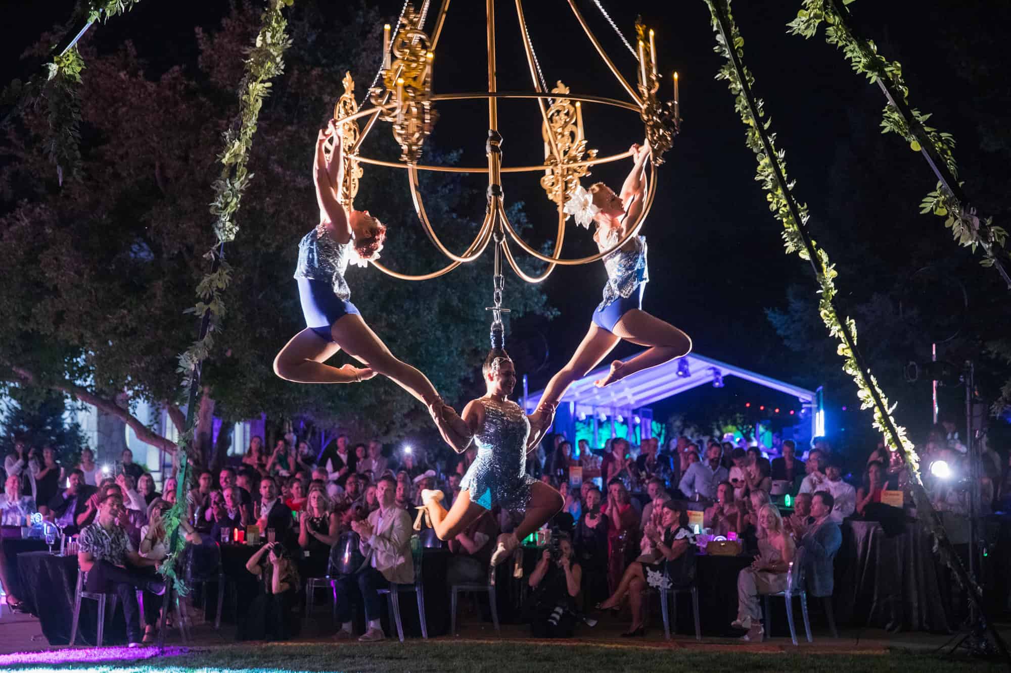 Performers hanging from a chandelier at a charity gala event.