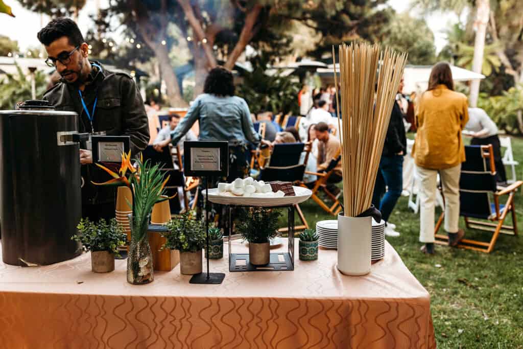 Outdoor event setup with a table of decorative items and guests in a garden setting.