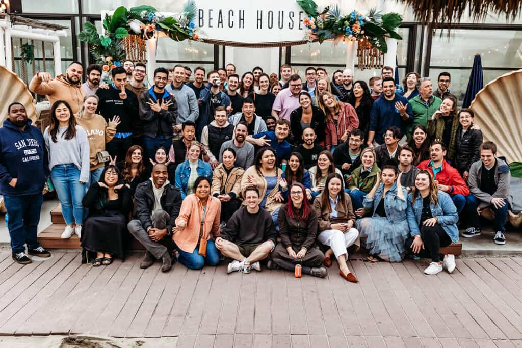 Group of people at a beach house event, smiling and waving for the camera.