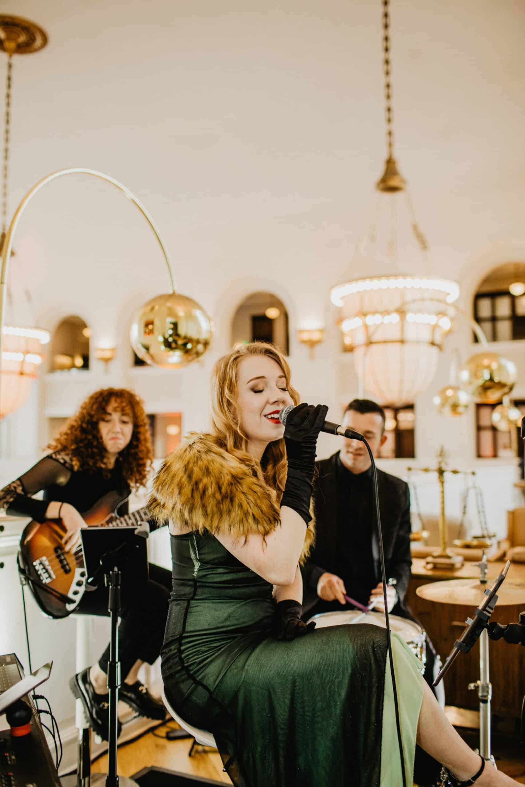 Live music performance at an elegant event space with chandeliers and gold decor.