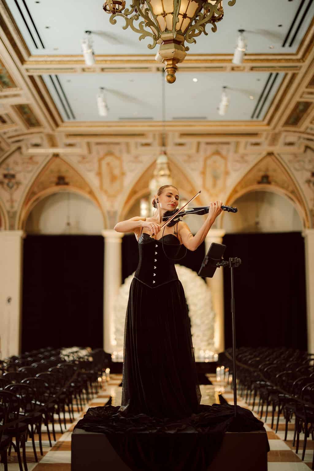 Female violinist performing at a luxury wedding ceremony in an ornate hall.