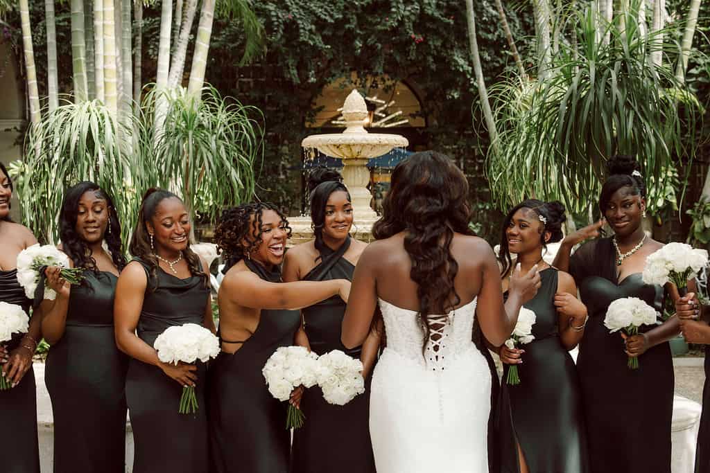 Bride with bridesmaids holding white bouquets in lush garden setting.