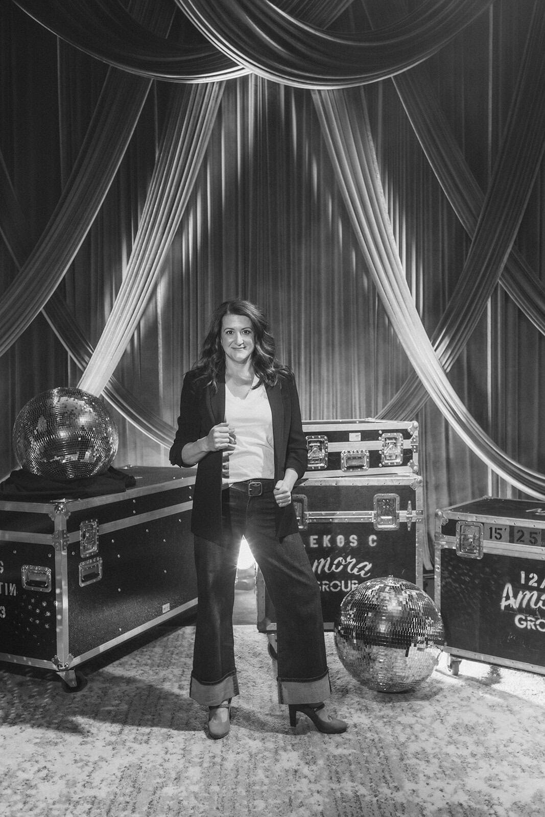 Woman standing at a corporate event with stage curtains and decorative spheres.
