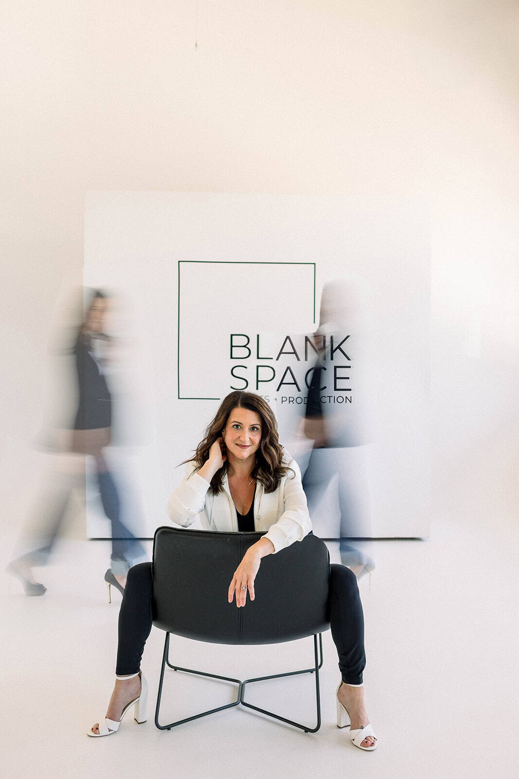 Woman sitting on a chair in front of a Blank Space Events backdrop with blurred people in motion.